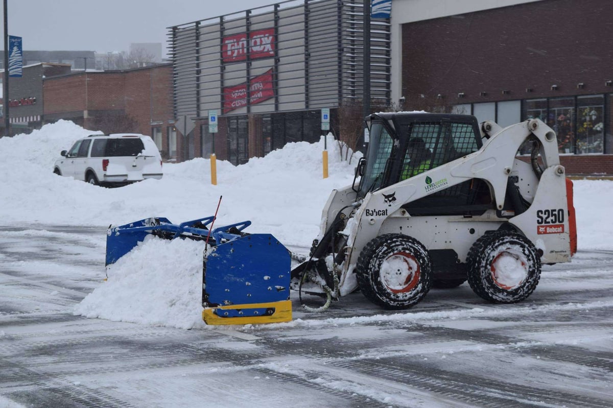 skid loader moving snow in commercial parking lot